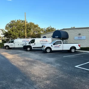 A side view of Strada Services building. White Strada Services vehicles are parked in front of the building.