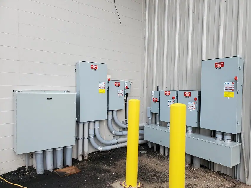 Two yellow poles stand in front of gray electrical boxes outside of a building.