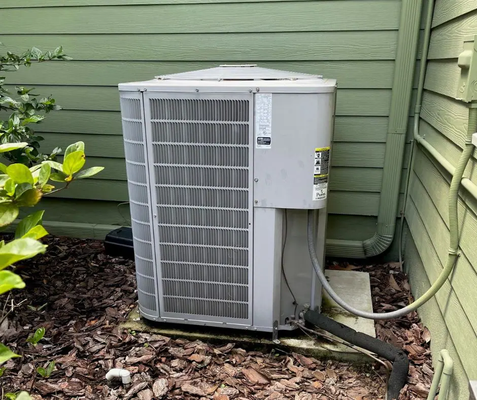 Running HVAC system next to a house with green siding.