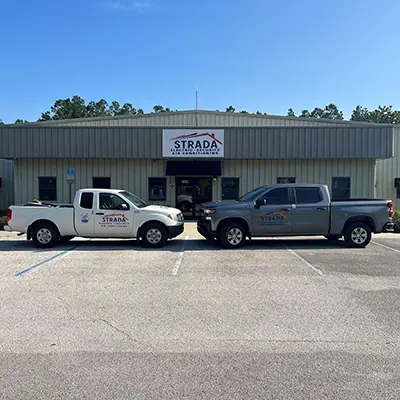 A white and a gray Strada Services pickup truck are parked facing each other in front of a building that has a Strada sign.